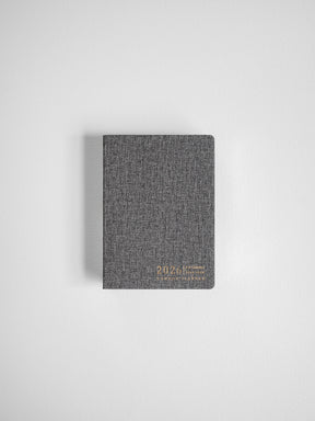 Compact, dark charcoal gray annual planner featuring a textured cover and clear 2026 inscription for full-year organization.