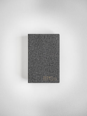 Dark gray, textured pocket daily planner cover printed with "2026" and "Daily Planner" in light lettering, ready for year-long scheduling.