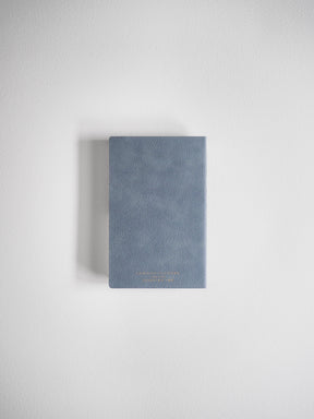Compact, dusty blue-gray planner with a smooth, minimalist cover and light embossed lettering detailing the full-year schedule.