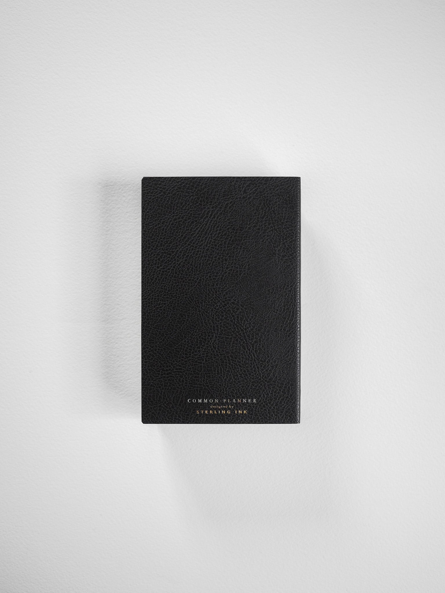 Compact, black faux-leather planner cover featuring debossed text branding, ideal for a sophisticated, full-year journal or pocket diary.