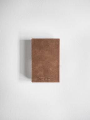 A vertical pocket planner crafted from textured, reddish-brown faux leather, featuring subtle gold debossing on the front cover.