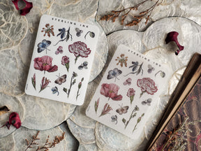 Botanical sticker sheets featuring detailed black and color illustrations of roses, irises, leaves, and stems in soft blush pink and deep burgundy tones.