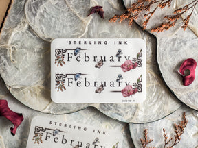 Elegant monthly sticker for February, featuring "Sterling Ink" text framed by delicate, faded botanical illustrations of soft pink and blue watercolor flowers.