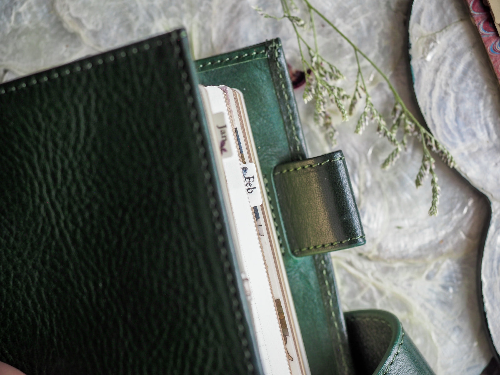 A detailed view of a dark green leather planner binder holding a white monthly tab labeled "Feb" for February 2024.