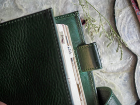 A detailed view of a dark green leather planner binder holding a white monthly tab labeled "Feb" for February 2024.