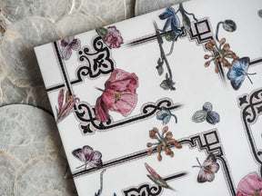 Elegant botanical pattern featuring watercolor renderings of pink poppies, blue blossoms, and brown clusters, framed by ornate black Victorian-style borders.