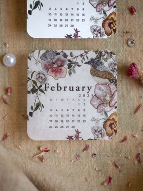 A beautiful botanical calendar sticker for February 2025, featuring watercolor illustrations of pink blossoms, lush green foliage, and a detailed bird motif.