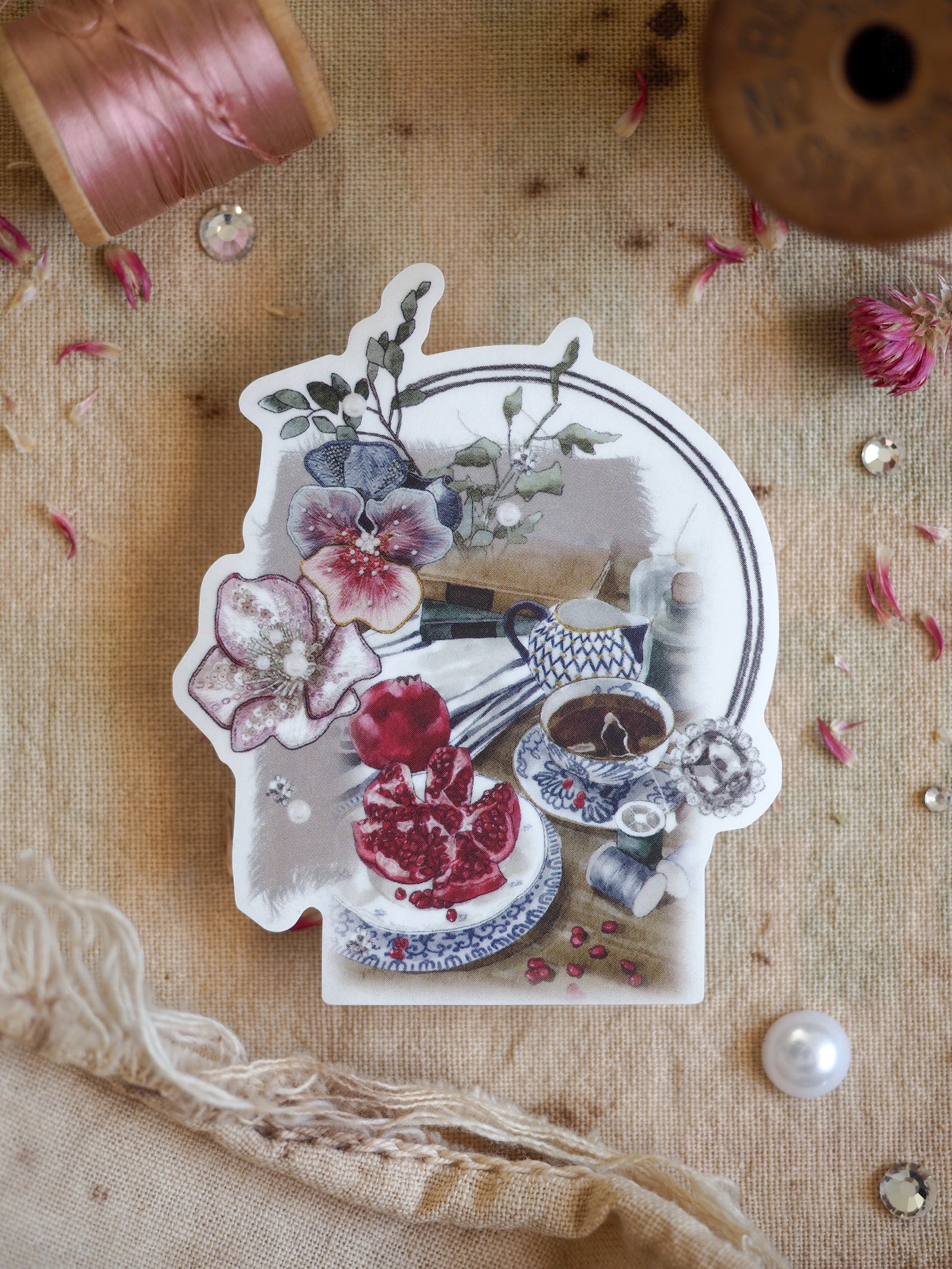 Vintage die-cut sticker of a romantic floral bouquet, showcasing pansies, deep pink roses, and a decorative teacup centerpiece.