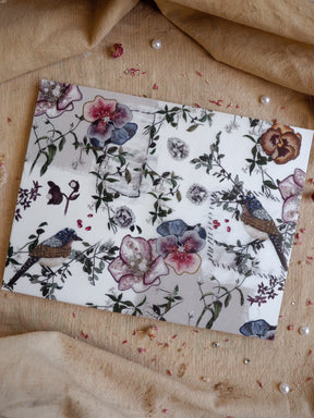 Elegant botanical print featuring watercolor flowers, lush foliage, and small birds, rendered in soft dusty purples and mauves.