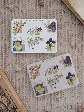 Lush, botanical-themed sticker sheets featuring watercolor depictions of deep indigo, lavender, and emerald flower clusters, labeled Sterling Ink.