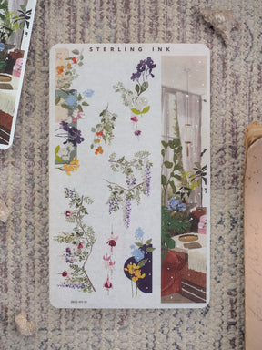 Botanical washi sticker sheet featuring delicate spring blossoms and foliage strips alongside an adjacent illustrated scene of a sunlit indoor garden.