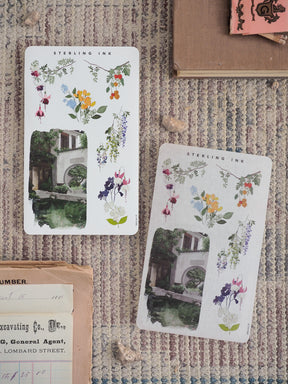 Pastel floral sticker sheets featuring a lush arrangement of lavender, lilac, and yellow wildflowers alongside a delicate stucco courtyard building.