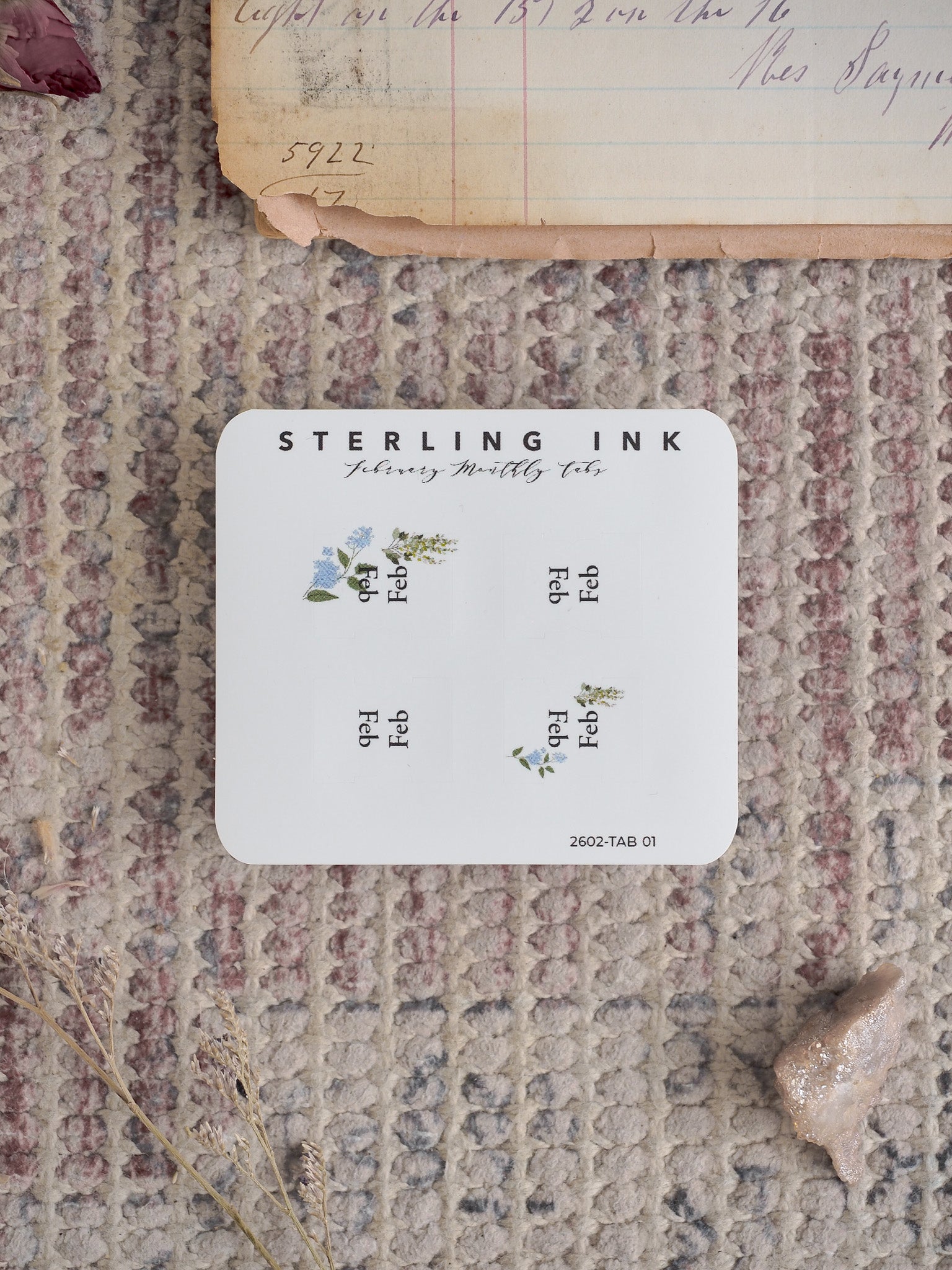 White planning tabs for February featuring "Sterling Ink" branding, organized with six labels and delicate watercolor sprigs of blue and white spring flowers.