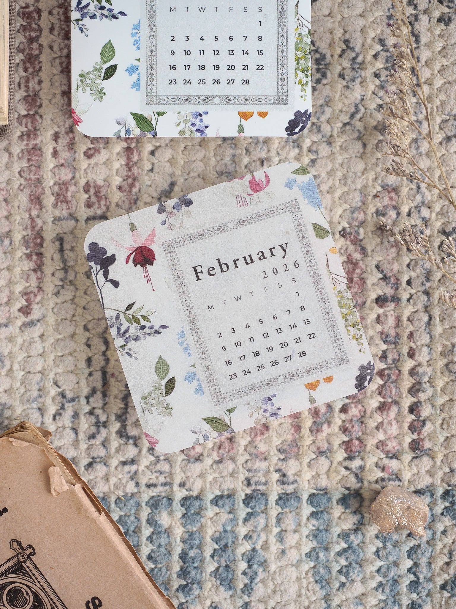 Decorative monthly calendar sheet for February 2026, framed by a delicate watercolor floral border featuring pink, blue, and green blooms.
