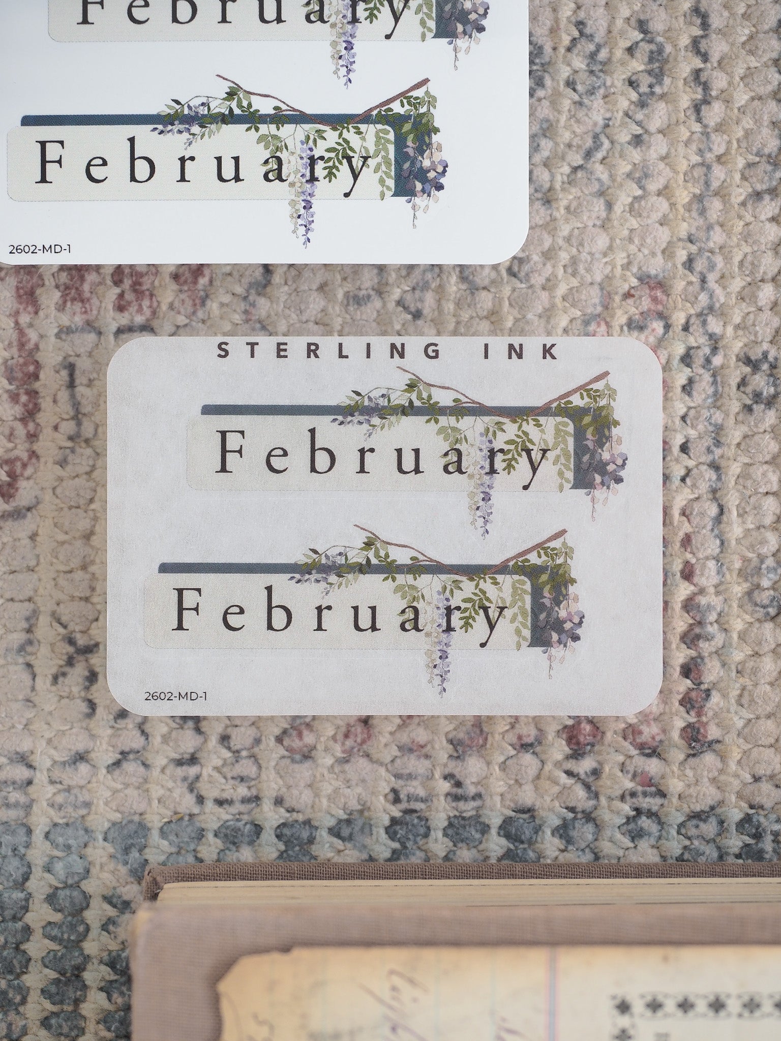 Set of elegant "February" month stickers featuring delicate purple and green watercolor floral vines and centered typography for seasonal journaling and planning.