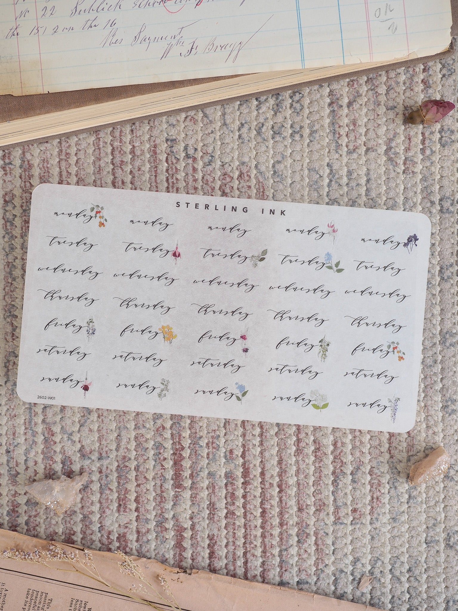 A decorative sticker sheet for February 2026, featuring the days of the week printed in deep maroon ink, surrounded by delicate, repeating floral and botanical motifs.
