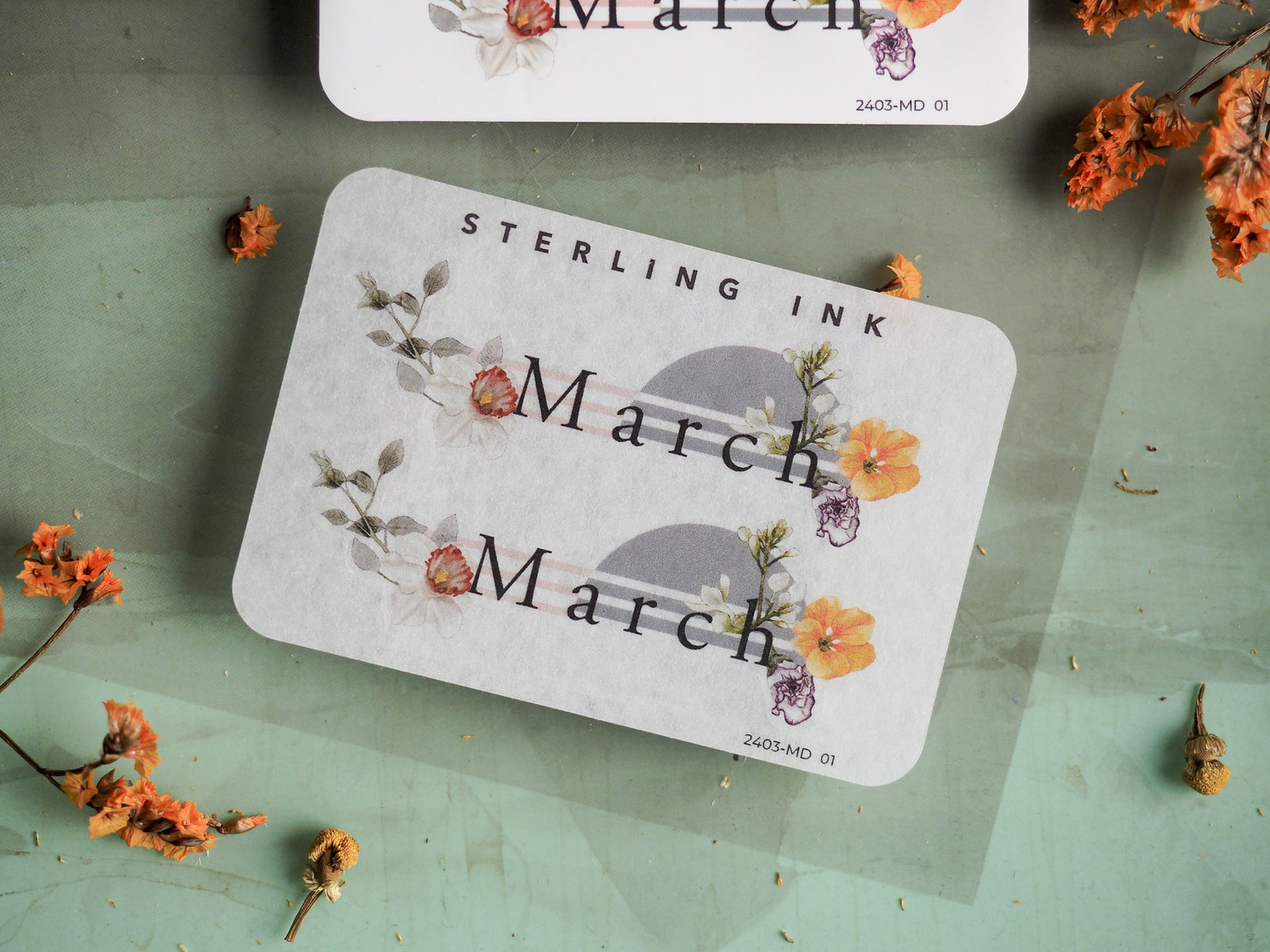 Decorative "March" month sticker featuring delicate watercolor botanical illustrations in soft pastel shades of yellow, pink, and gray.