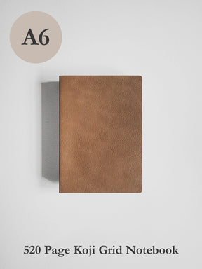 A6 size brown textured leather notebook cover shown closed on a light gray background, with text indicating it is a 520 page Koji Grid Notebook.
#Color_Caramel