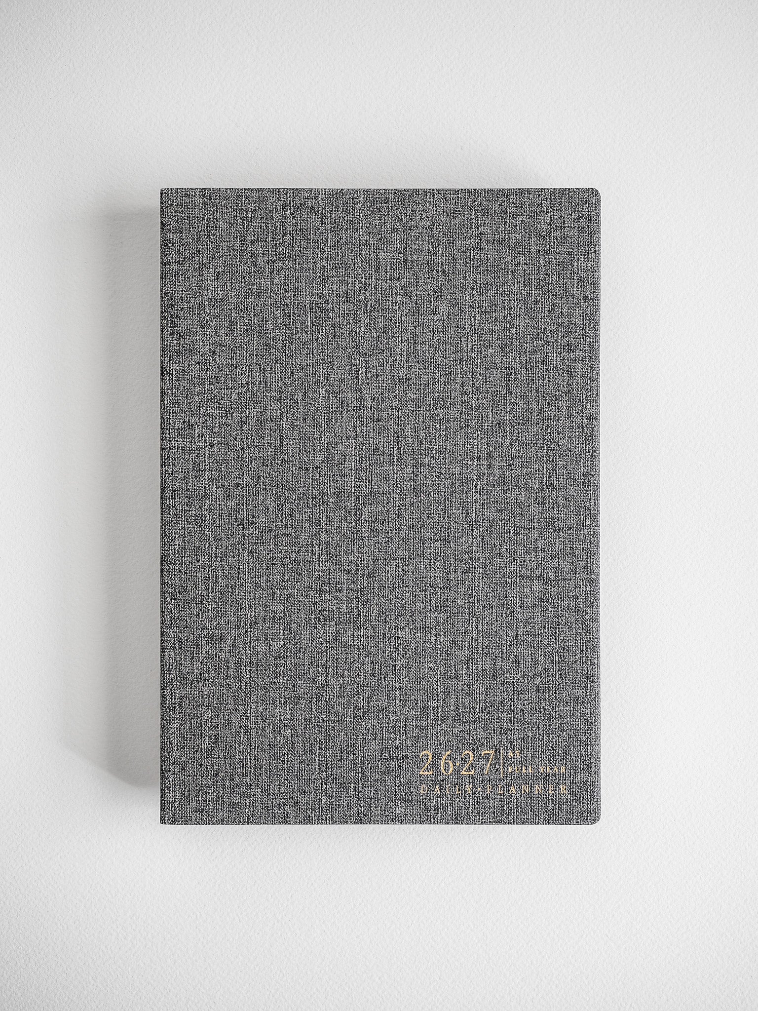 Minimalist daily planner featuring a textured, speckled charcoal grey cover with subtle metallic lettering for the 2026-2027 academic year.