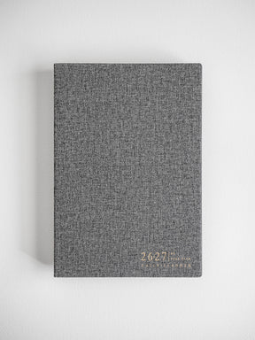 Minimalist daily planner featuring a textured, speckled charcoal grey cover with subtle metallic lettering for the 2026-2027 academic year.