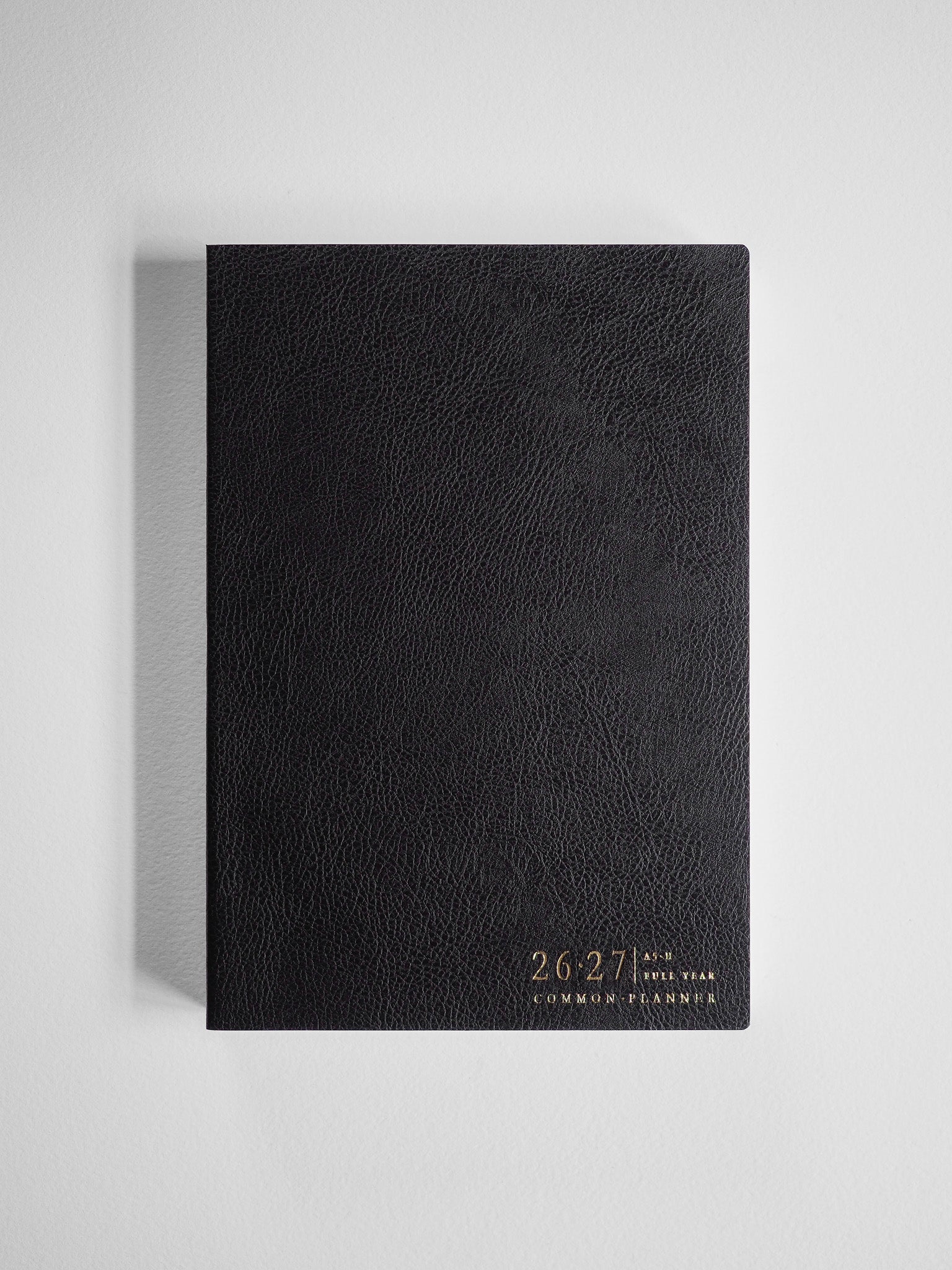 Black academic planner with a textured faux leather cover, featuring the years "26-27" and "Common Planner" printed in elegant gold lettering.