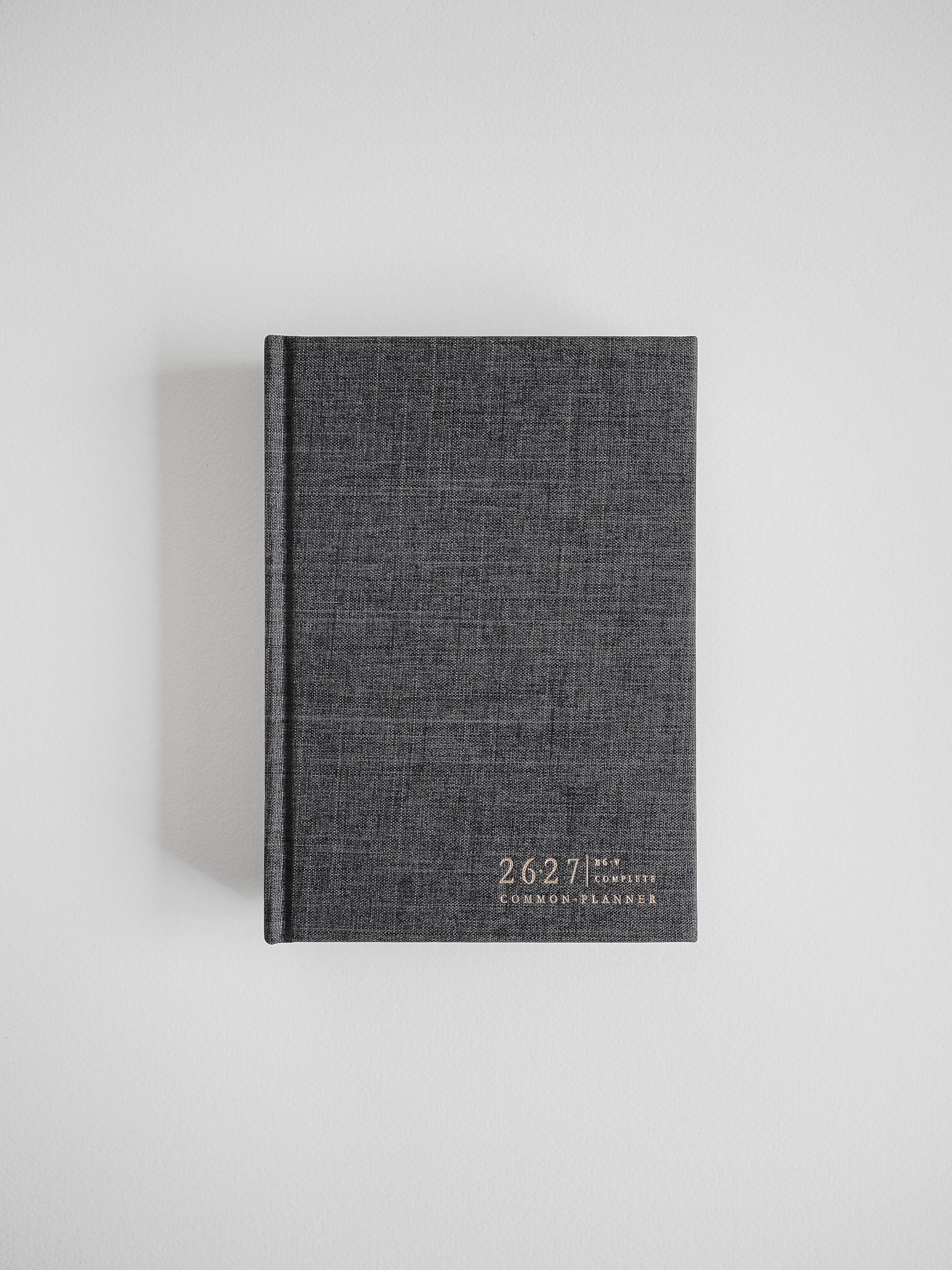 Dark charcoal B6 academic planner featuring a woven textured cover and minimalist white branding for the 2026-2027 Common Planner.