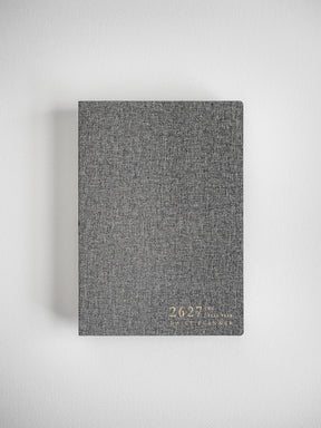Textured B6 daily planner with a charcoal gray woven cover, clearly displaying the "2026-2027" academic year dates for organization.
