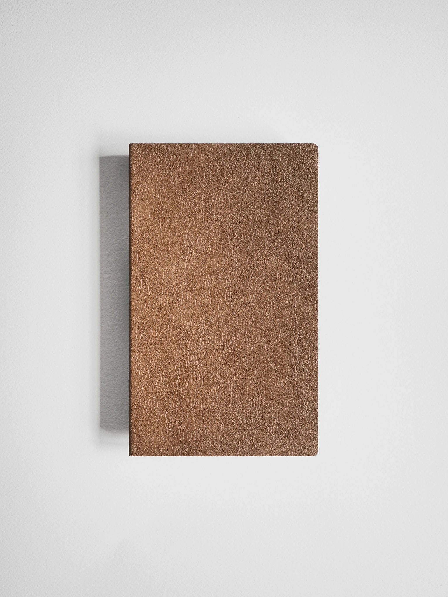 A brown textured leather notebook or journal with a visible gray spine, photographed from above on a clean white background.
#Color_Caramel