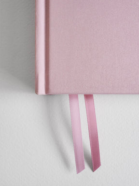 Pale pink B6 vertical planner journal featuring a solid blush cover and tied with two matching pale pink satin ribbon bookmarks.