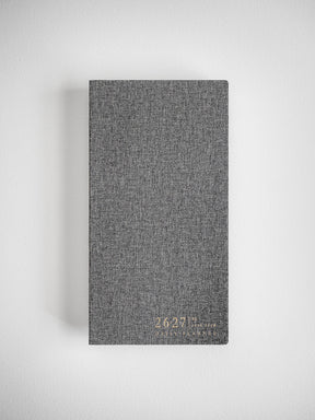 Sophisticated daily planner cover in a textured, dark charcoal gray fabric, subtly marked with academic branding for the 2026–2027 school year.