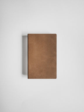 A brown textured leather notebook or journal with a pebbled leather cover, shown closed against a neutral light gray background.
#Color_Caramel