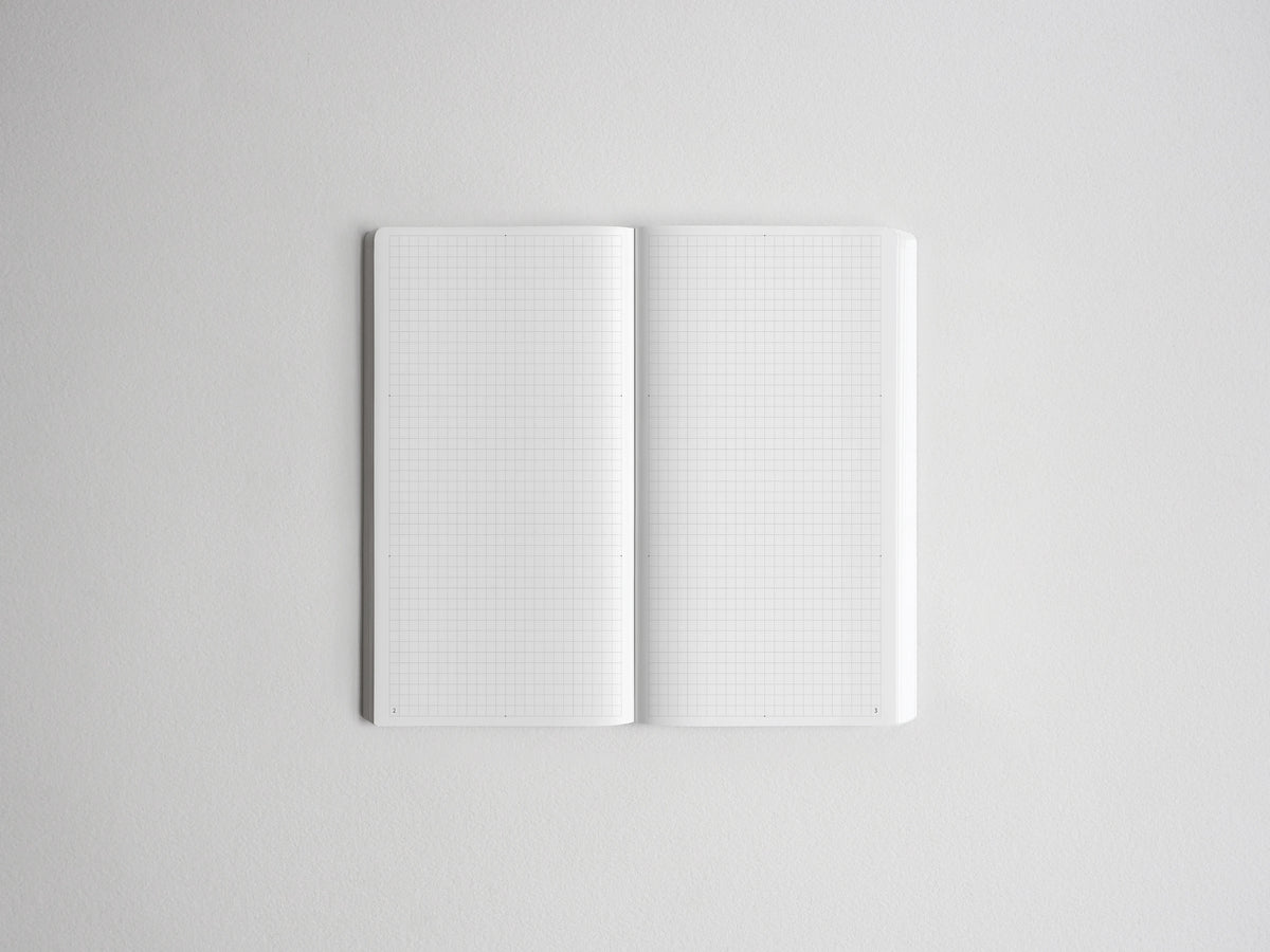 An open notebook with white grid paper pages, centered on a light gray background.