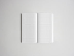 An open notebook with white grid paper pages, centered on a light gray background.