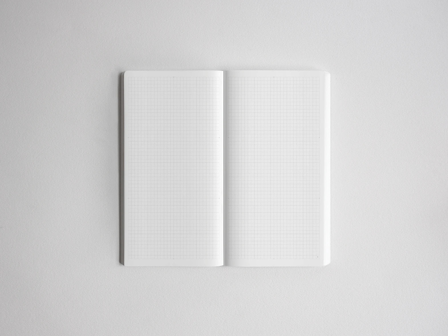 An open notebook with two blank white grid pages, photographed from above on a light gray background.