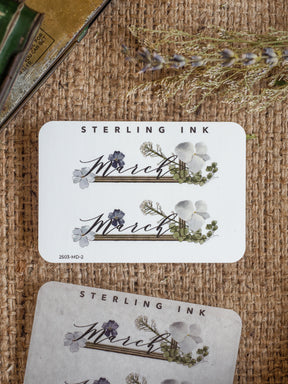 Elegant March sticker set featuring a muted watercolor floral wreath of white and purple blossoms surrounding the month's name.