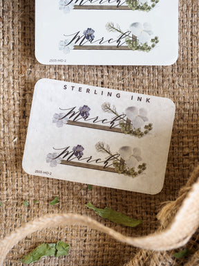 Charming March month sticker set featuring elegant script calligraphy framed by delicate watercolor purple and white spring florals.