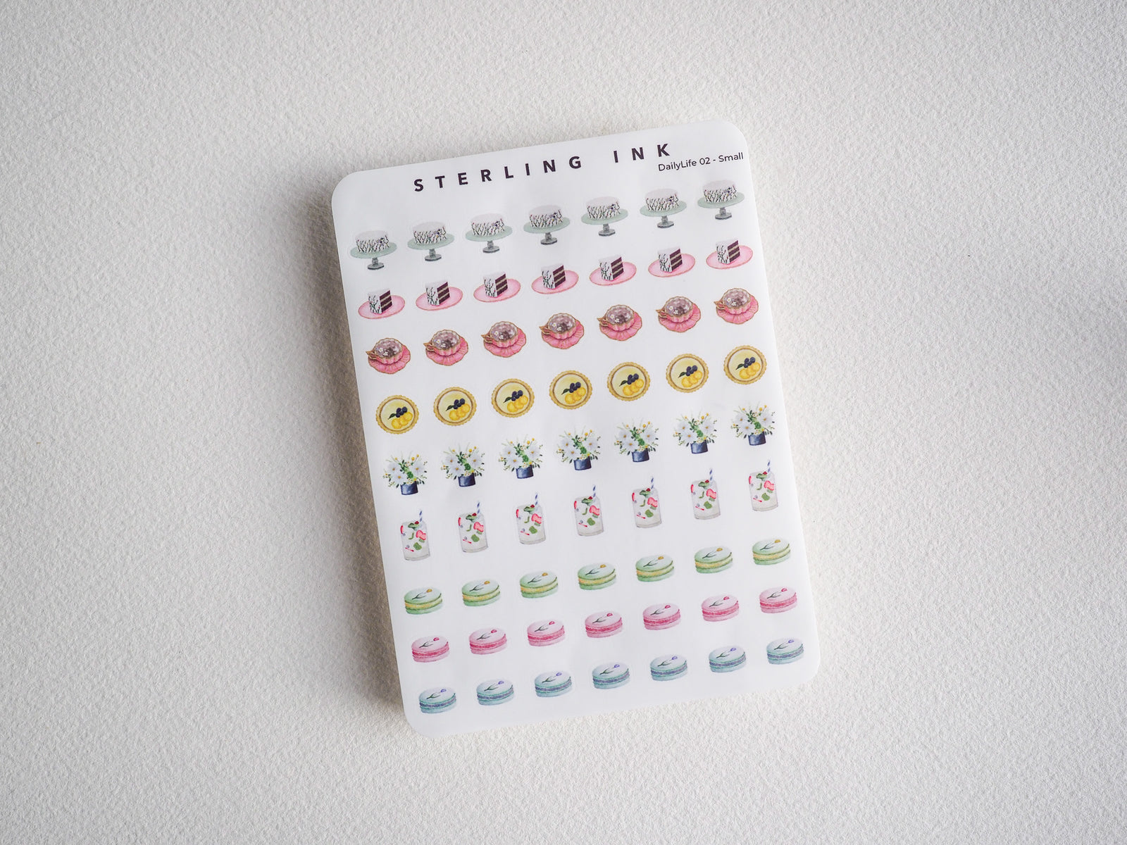 Pastel enamel pin stickers featuring cute motifs: pink pastries, yellow florals, small potted plants, and pastel rainbow