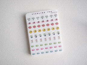 Pastel enamel pin stickers featuring cute motifs: pink pastries, yellow florals, small potted plants, and pastel rainbow