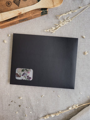 Matte black journal cover featuring a subtle, elegant floral insert of pressed botanicals in shades of deep purple and forest green.