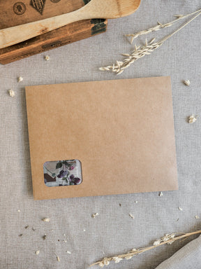 Rustic kraft paper envelope holding a delicate floral insert featuring purple and muted spring blossoms for the March 2026 kit.