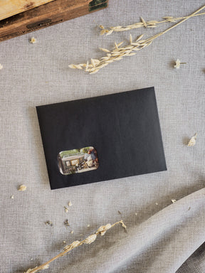 Sleek black card sleeve featuring a warm, nostalgic photograph of people enjoying an outdoor cafe setting, marking the March 2026 subscription kit.