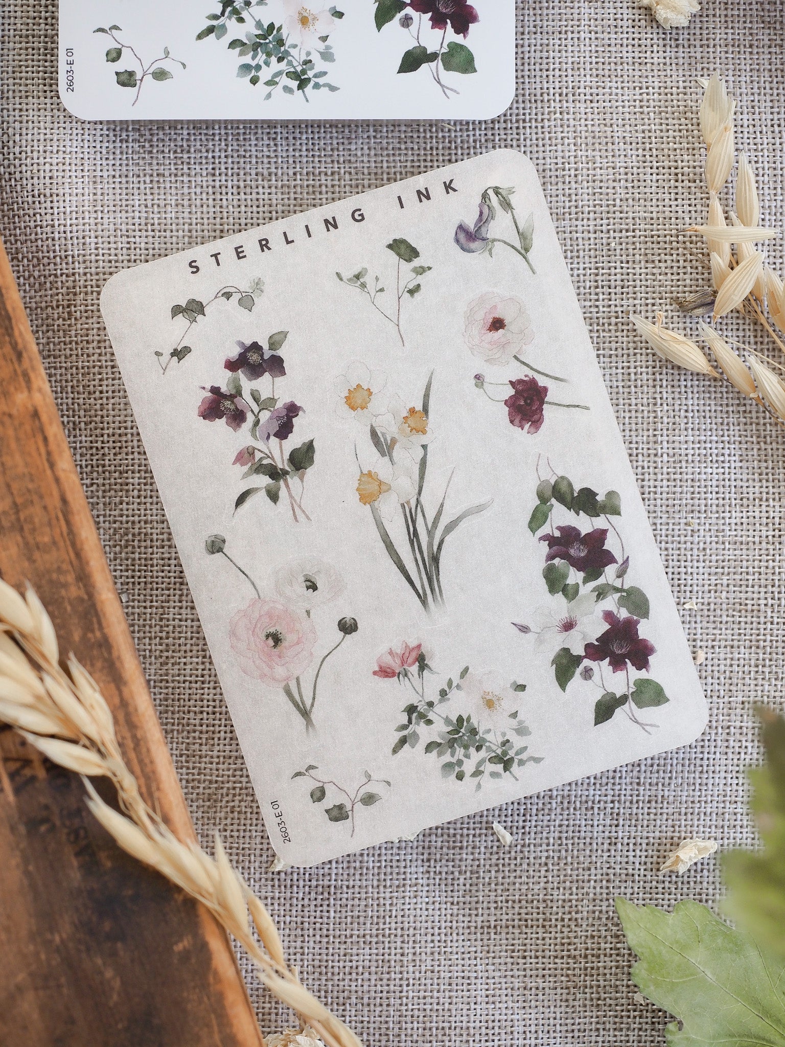Delicate sticker sheet featuring a rich watercolor arrangement of assorted purple and pink botanical flowers and foliage, labeled "Sterling Ink."