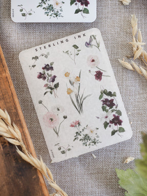 Delicate sticker sheet featuring a rich watercolor arrangement of assorted purple and pink botanical flowers and foliage, labeled "Sterling Ink."