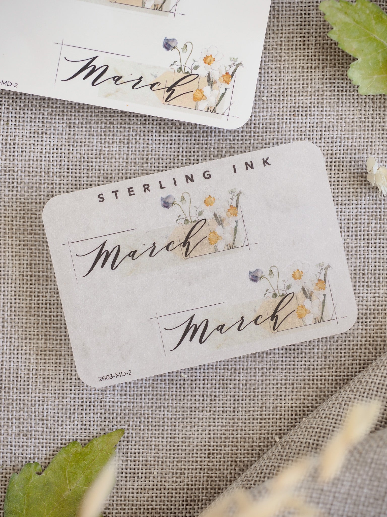 Watercolor floral month sticker for March, featuring elegant script, delicate yellow and purple spring blooms, and detailed line work for journaling or planner decorating.