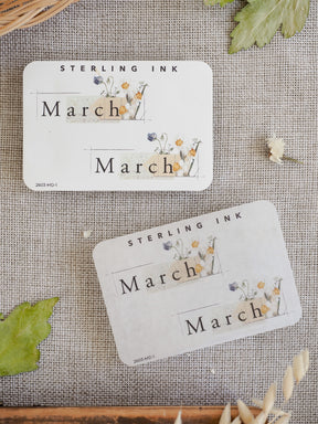 Spring-themed "March" sticker featuring delicate watercolor florals, greenery, and soft pastel accents on an off-white background.