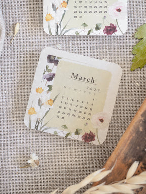A lovely March 2026 monthly calendar featuring a delicate design of pink and purple watercolor flowers and greenery on a creamy background.