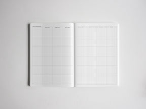 Open white grid notebook spread detailing structured planning sections for daily, monthly, quarterly, and yearly goal breakdowns.