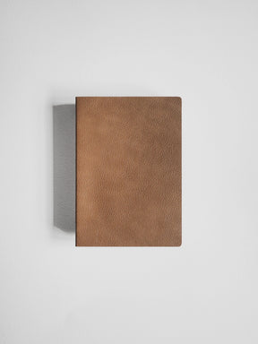 A brown textured leather notebook or journal with rounded corners, shown closed against a light gray background with a soft shadow to the left.
#Color_Caramel