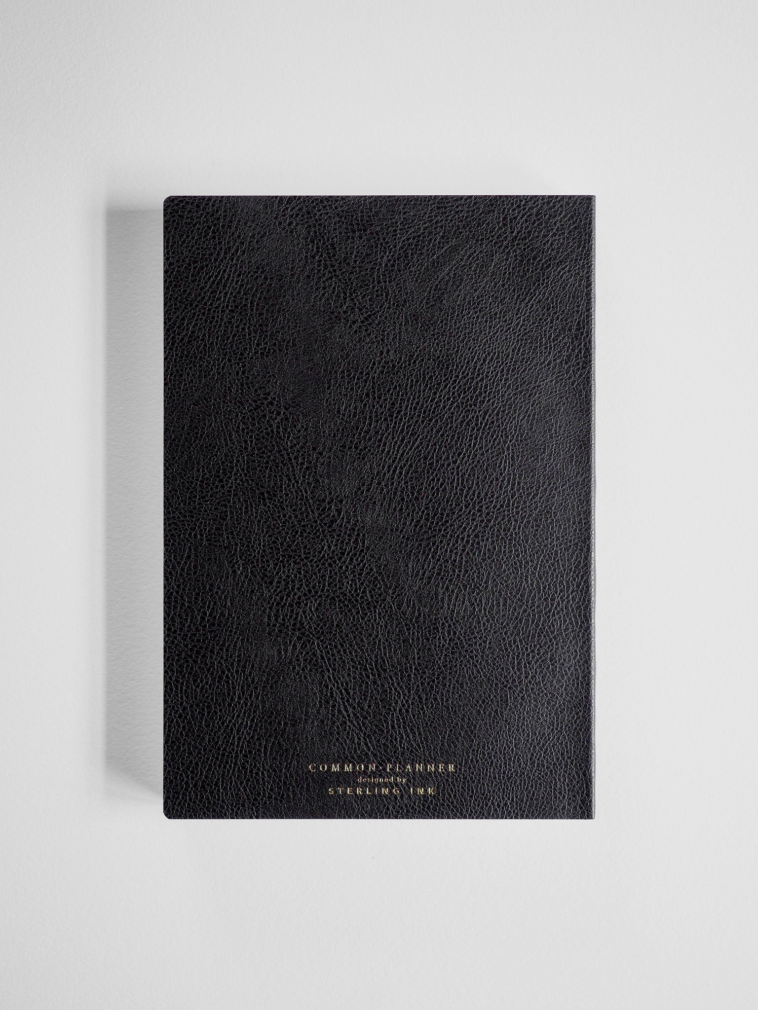 Structured black planner cover with a subtle faux leather grain and centered gold foil branding for the Common Planner brand.