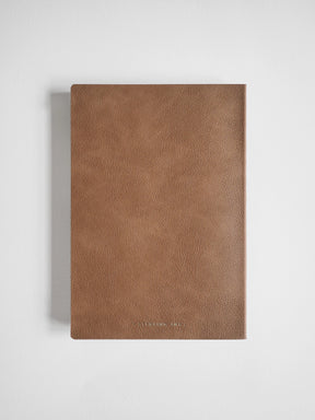 A brown textured leather notebook or journal with a minimalist design, shown closed on a light gray background.
#Color_Caramel